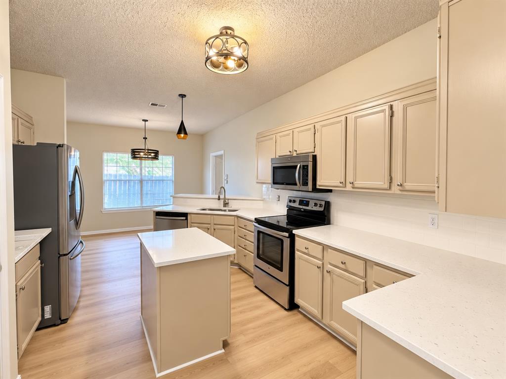Kitchen featuring custom cabinetry, light-toned countertops, stainless steel appliances, a mobile center island, and wood-finish flooring