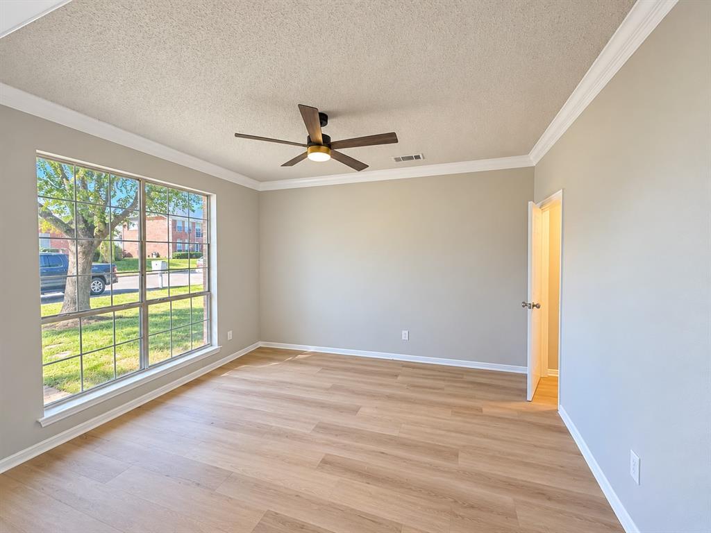 Wood-finish flooring, crown molding, a large picture window, and a ceiling fan with integrated lighting