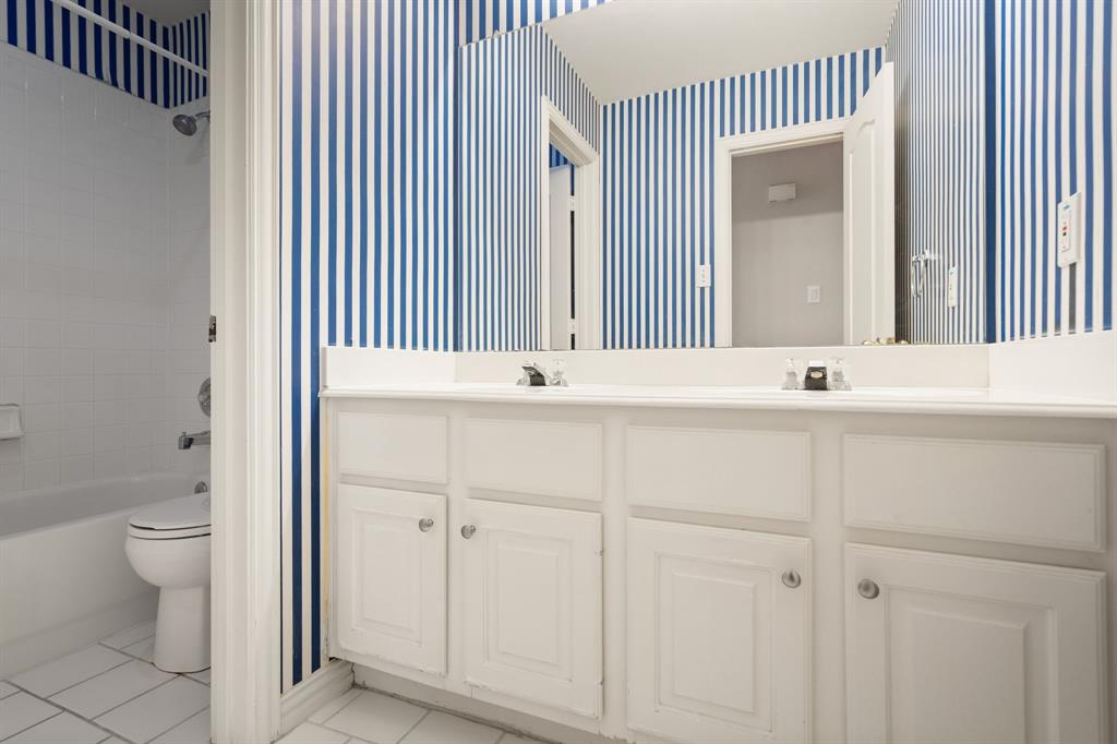 Full bath featuring tile patterned floors, wallpapered walls, double vanity, and shower / bath combination