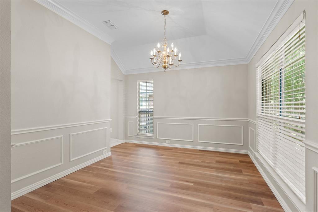 Unfurnished dining area featuring a chandelier, crown molding, light wood finished floors, a decorative wall, and a wainscoted wall