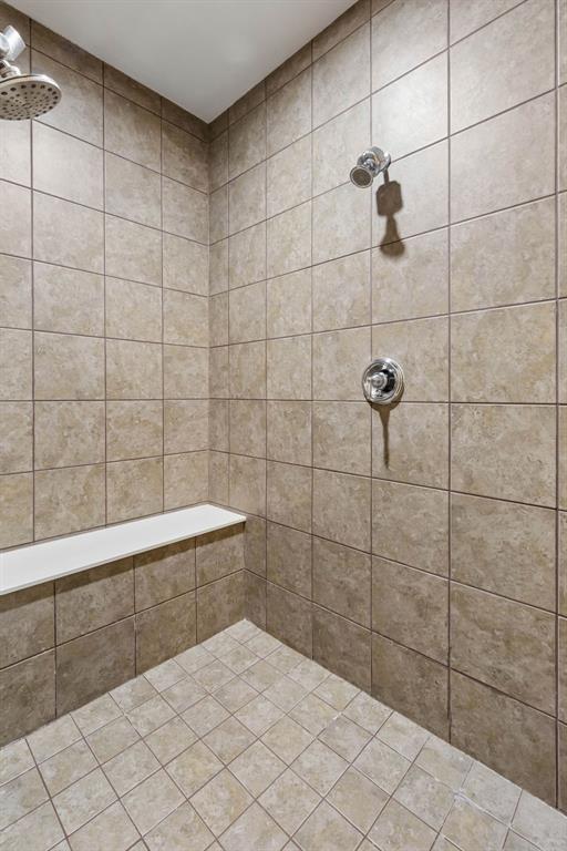 The spacious walk-in shower features a built-in bench, beautiful tile finishes, sleek chrome fixtures, and dual shower heads for added comfort.