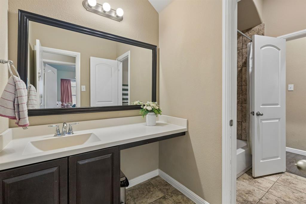 The guest bath features generous counter space, stained wood cabinets, a framed mirror, and tile flooring. A separate door provides privacy for the tub and shower area, with convenient access from the hallway leading to the media room and additional living spaces.