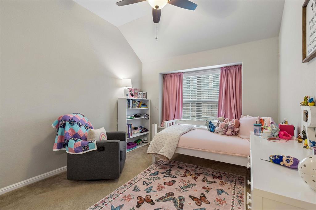 The first secondary bedroom features cozy carpeting, a ceiling fan, a charming window seat, a large window for natural light, and a beautiful arched ceiling.
