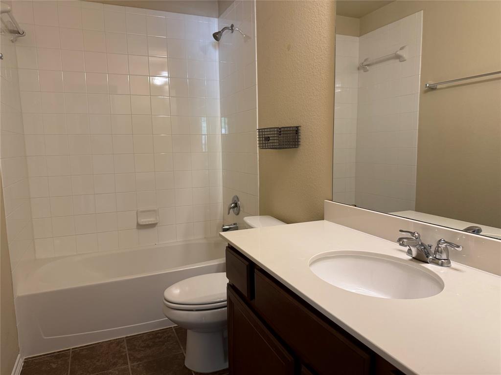 Bathroom featuring a vanity with a light-toned solid surface countertop, an integrated oval sink, dark cabinetry, ceramic tile bathtub surround, and tile flooring