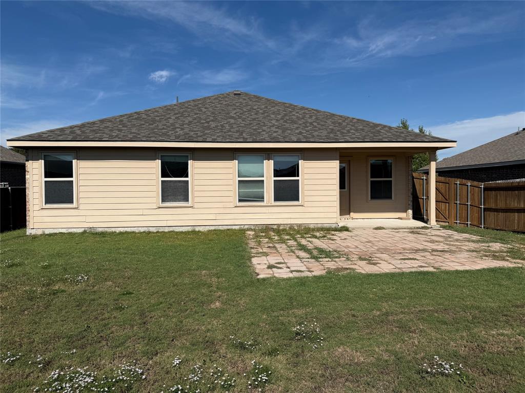 Rear elevation featuring horizontal lap siding, a hipped roof, covered patio area, concrete paver patio, and wood privacy fencing