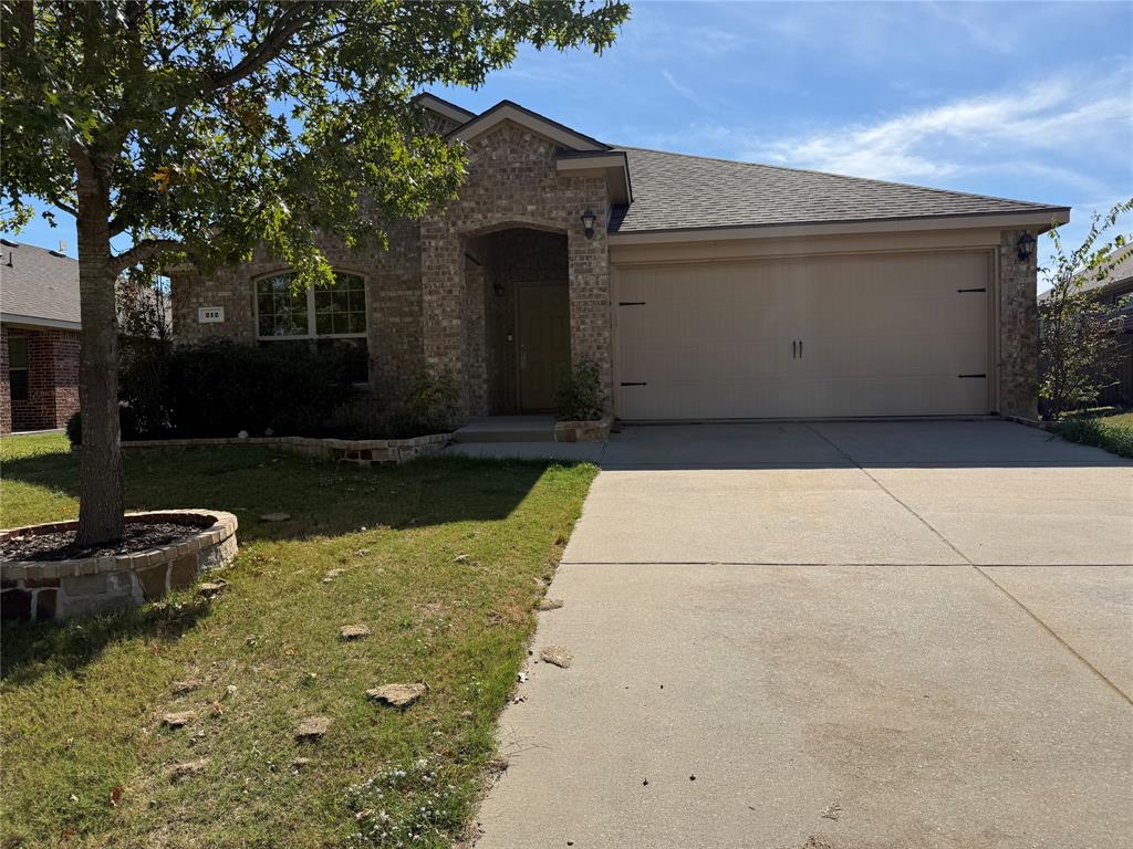 Brick veneer facade with an arched entryway, recessed front door, two-car garage, and stone-bordered landscaping