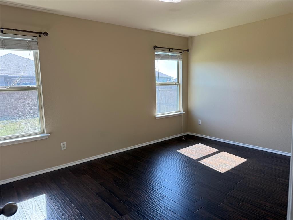 Room featuring dark wood-finish flooring, neutral-toned walls, and two double-hung windows with installed curtain rods