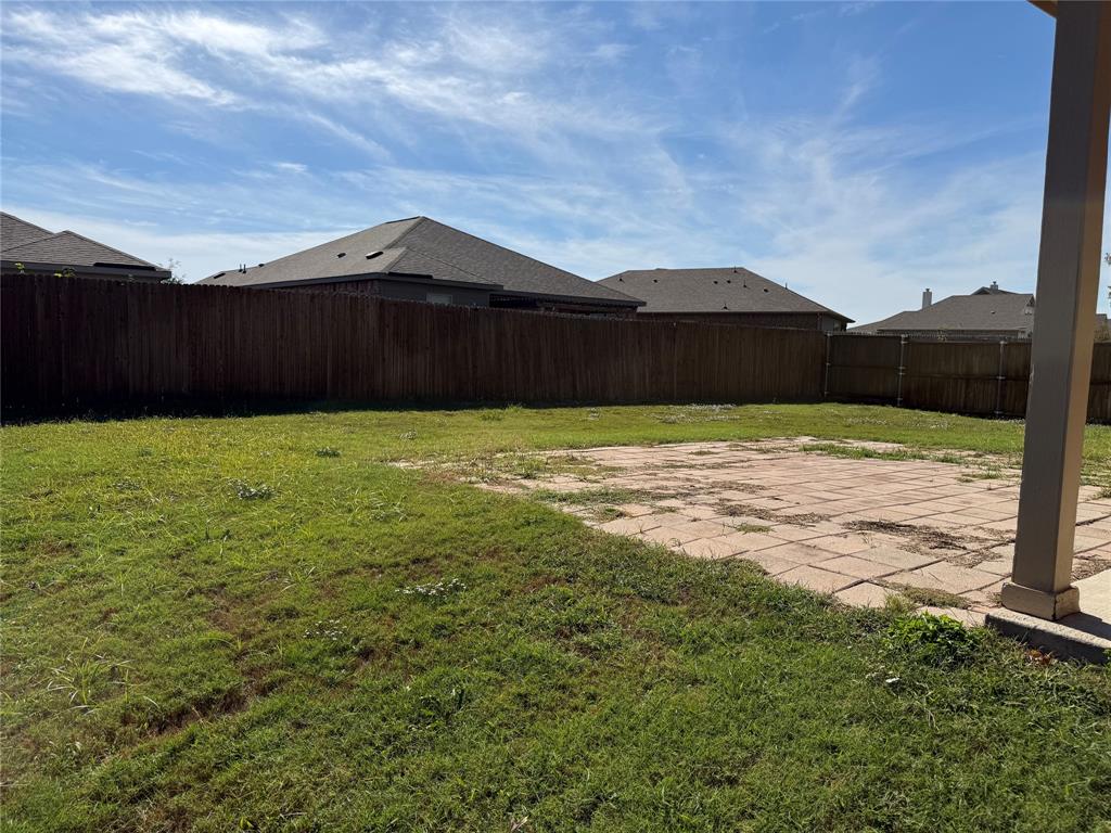 Backyard featuring a paved stone patio, wood privacy fencing, and a grass lawn