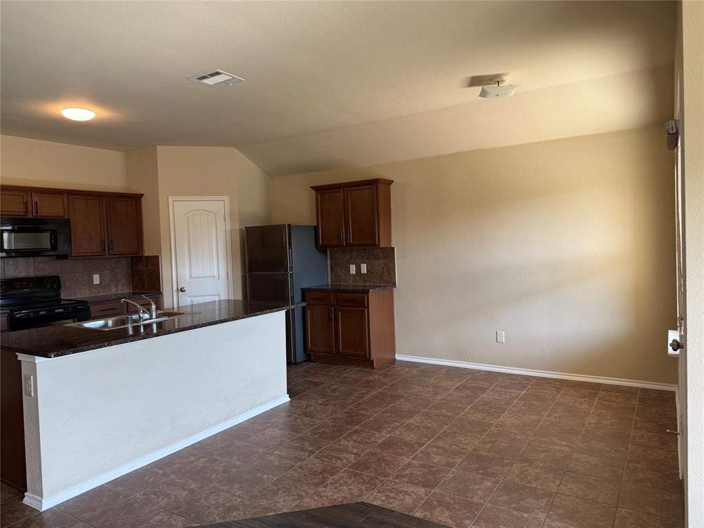 Kitchen featuring stained wood cabinetry, stone-finish countertops, tile flooring, and a peninsula island with an integrated stainless steel sink