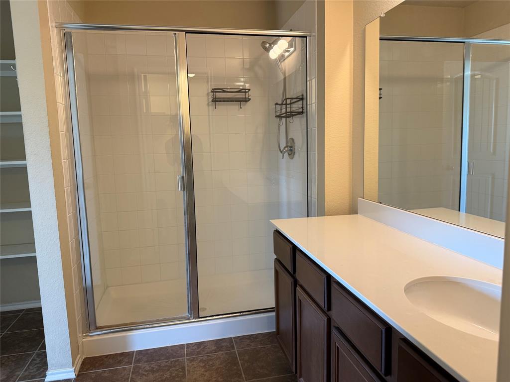 Bathroom featuring a vanity with a white countertop and integrated sink, a glass-enclosed shower with tiled walls, built-in shelving, and dark-toned cabinetry