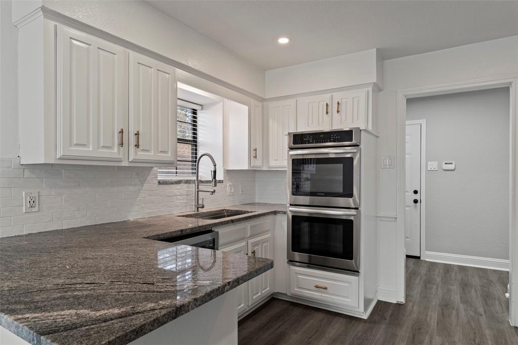 Kitchen featuring granite countertops, white cabinetry with metallic hardware, subway tile backsplash, stainless steel double wall oven, and wood-finish flooring