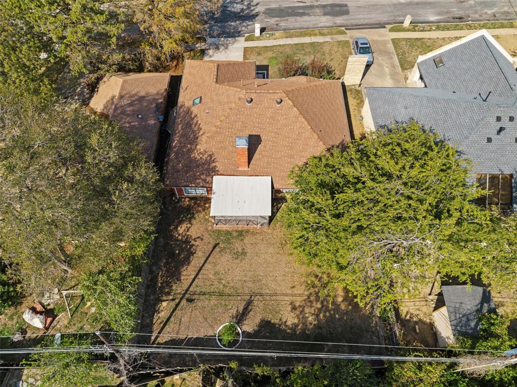 Aerial perspective of the residential lot featuring a multi-slope roofline, a centered masonry chimney, a screened rear patio structure, and mature tree coverage