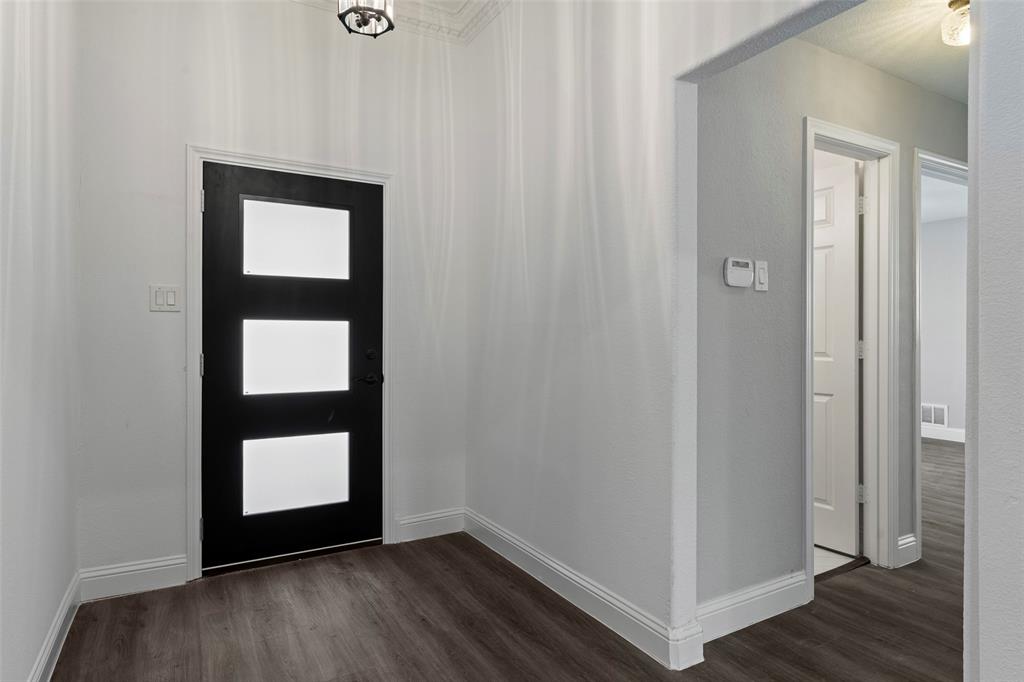 Entryway featuring a black exterior-style door with three rectangular glass inserts, wood-finish flooring, neutral wall paint, and overhead decorative lighting