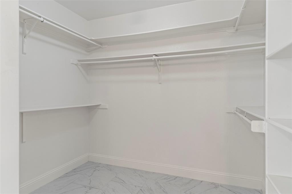 Walk-in closet featuring multi-level built-in shelving, white overhead hanging rods, and patterned tile flooring