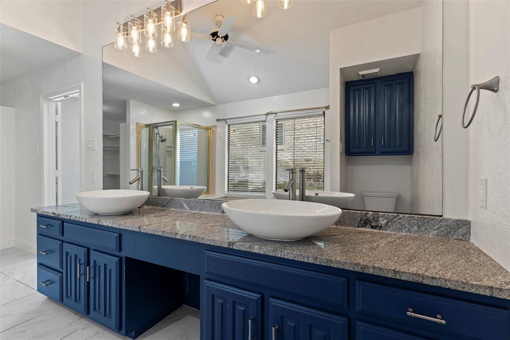 Dual vanity featuring navy blue cabinetry, stone countertops, vessel sinks, chrome faucets, and a full-width mirror