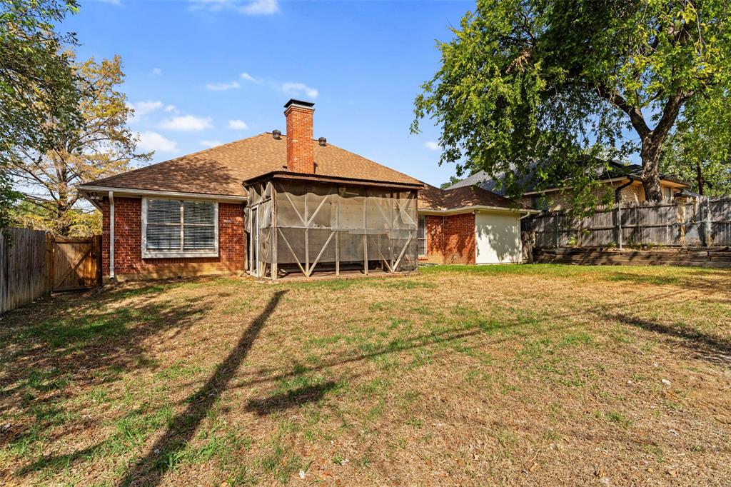 Exterior backyard featuring a brick facade, screened porch, brick chimney, wood fence, and mature trees