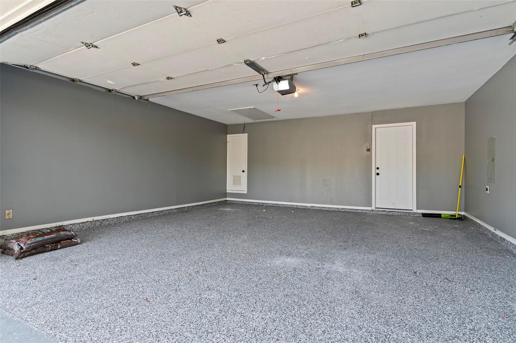 Finished garage space featuring durable epoxy flooring, neutral wall paint, a metal panel overhead garage door, and a dedicated entry door