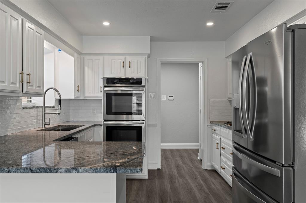 Kitchen featuring white cabinetry with metallic pulls, granite countertops, stainless steel double wall ovens, stainless steel refrigerator, and wood-finish flooring