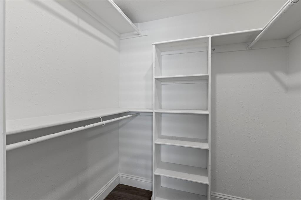 Walk-in closet featuring white built-in shelving, dual-level hanging rods, and dark wood-finish flooring