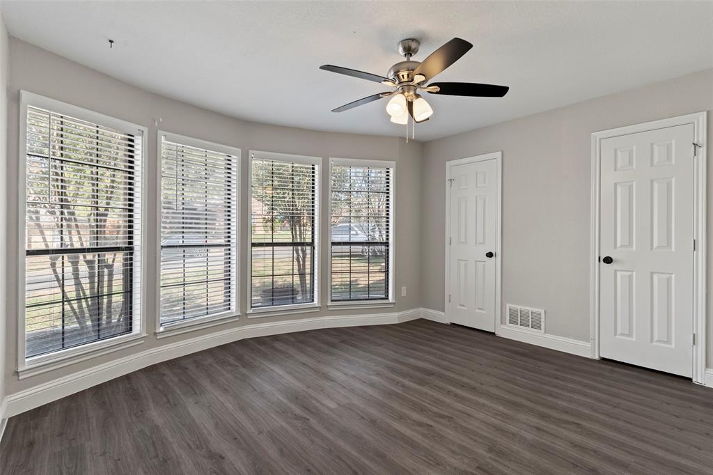 Room featuring wood-finish flooring, a four-panel bay window configuration, and a multi-blade ceiling fan with integrated lighting