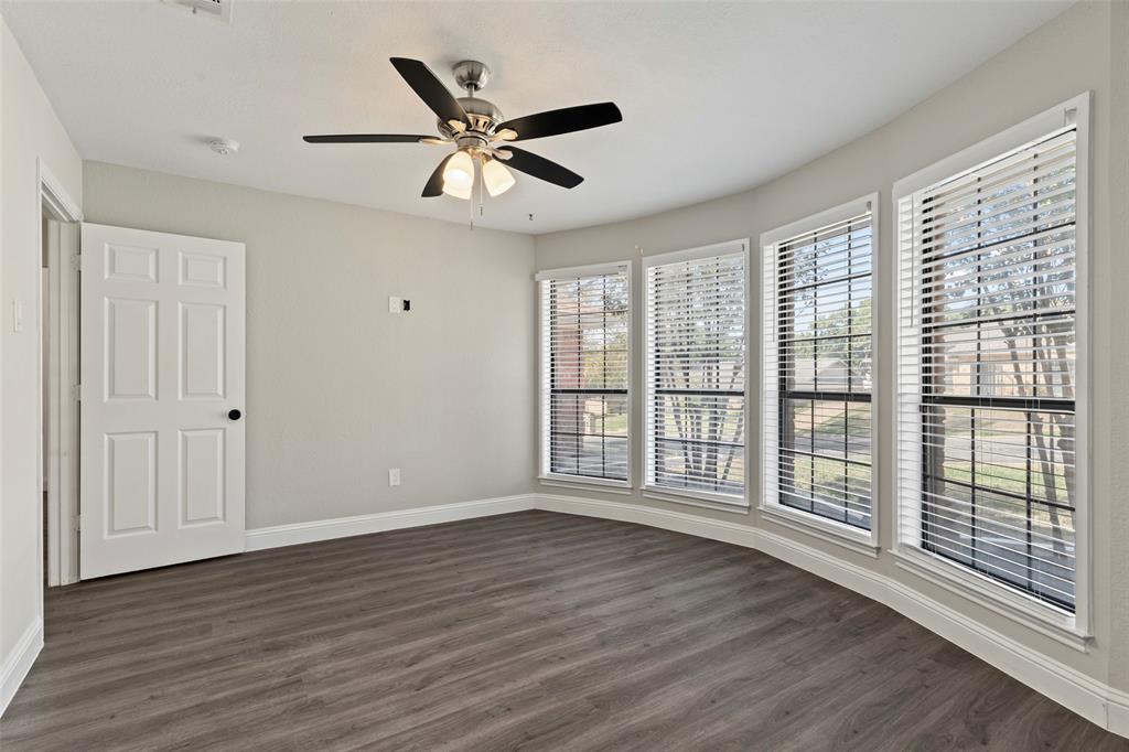 Bay window featuring four windows, wood-finish flooring, brushed nickel ceiling fan with integrated lighting, and a six-panel interior door