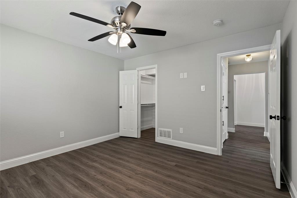 Neutral-toned interior featuring wood-finish flooring, a multi-blade ceiling fan with integrated lighting, a six-panel door, and a built-in walk-in closet