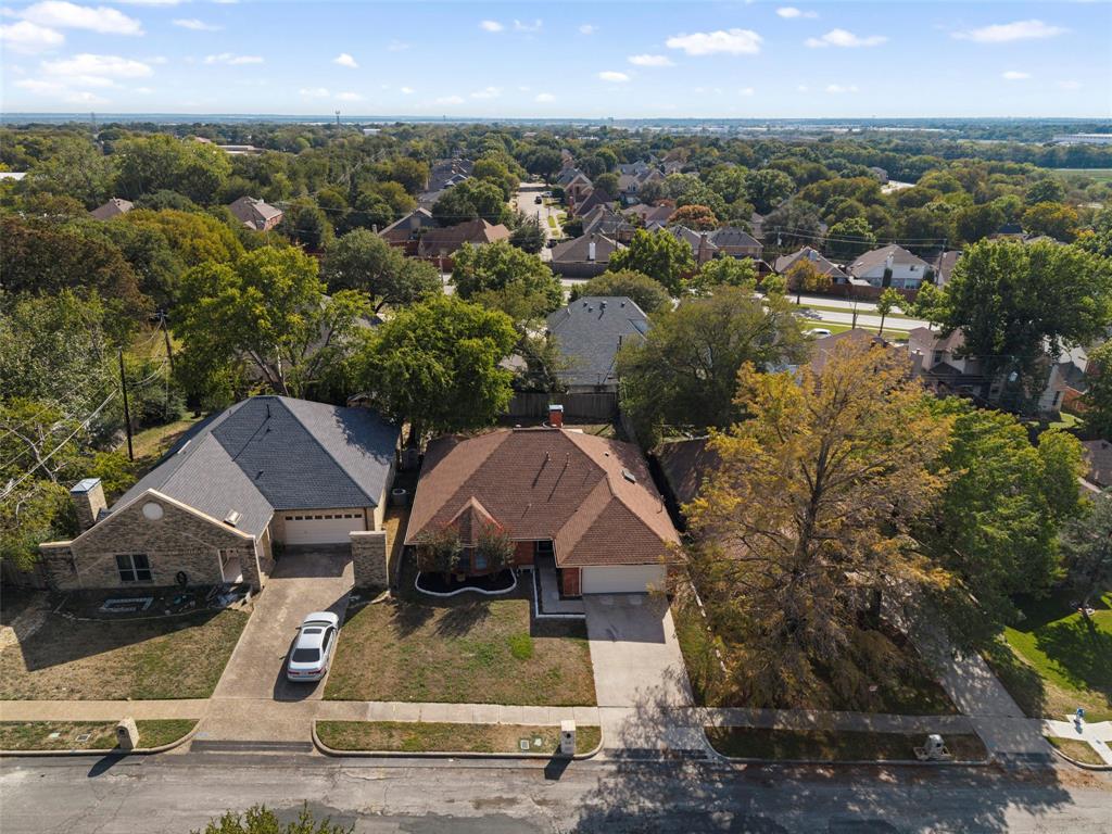 Aerial perspective of residential properties featuring brick and masonry construction, multi-pitched shingle roofs, attached multi-car garages, concrete driveways, and established tree canopy