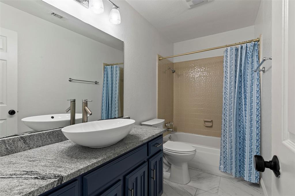 Bathroom featuring a vanity with dark-finish cabinetry, stone countertop, and an oval vessel sink, complemented by stone-patterned tile flooring and a tiled shower surround