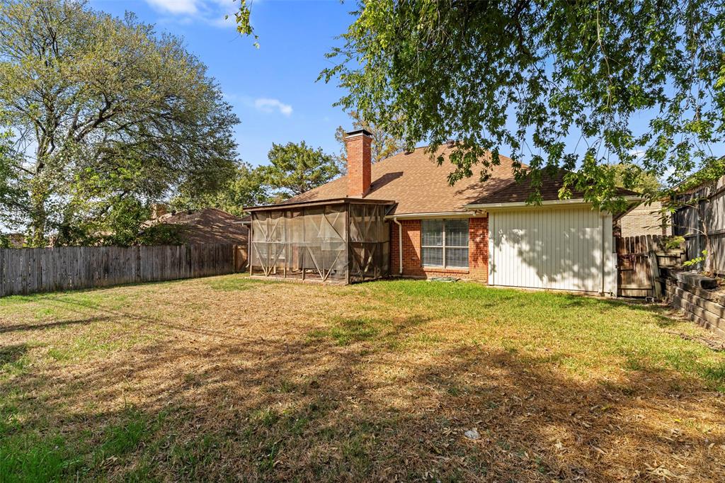 Rear exterior featuring a brick chimney, screened-in porch, composition shingle roof, wood privacy fencing, and a retaining wall