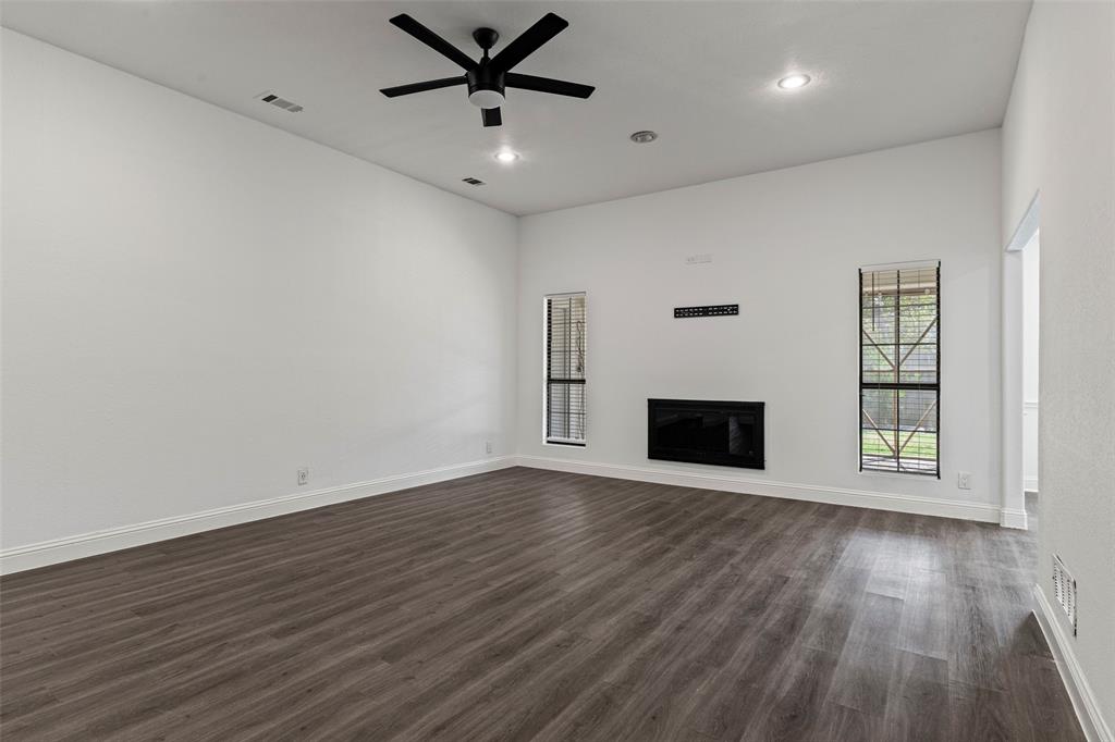 High-ceilinged room featuring wood-finish flooring, a flush-mount fireplace, dual windows with grid detailing, and a matte black ceiling fan