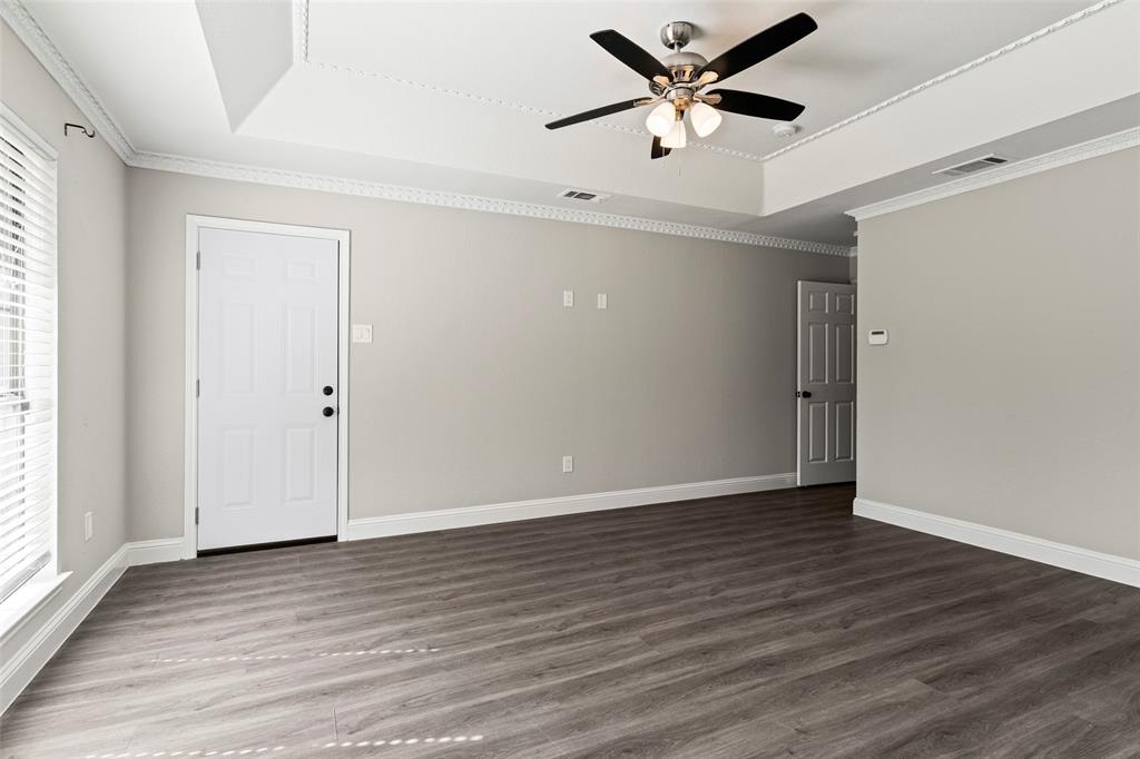 Tray ceiling with crown molding, wood-finish flooring, and a central ceiling fan with integrated lighting
