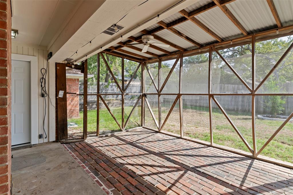 Screened patio featuring a herringbone-patterned brick floor, exposed timber framing, corrugated metal ceiling, and a ceiling fan