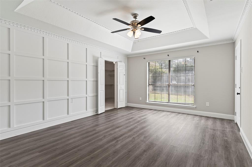 Interior space featuring a recessed tray ceiling, wood-finish flooring, decorative wall molding, and a central ceiling fan with integrated light fixture