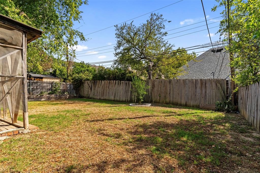Backyard featuring a wood-panel fence, mature trees, a screened-in structure, and open green space