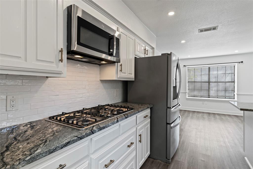Kitchen featuring white shaker-style cabinetry, granite countertops, a subway tile backsplash, a built-in stainless steel microwave, and wood-finish flooring