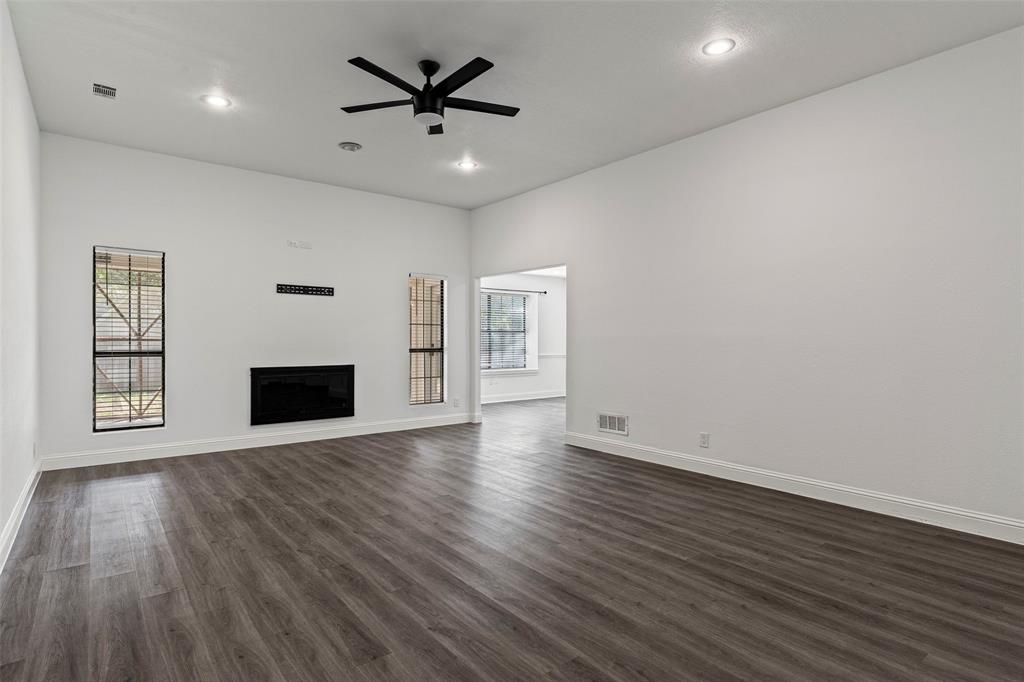 Spacious interior featuring wood-finish flooring, high ceilings with recessed lighting, a matte black ceiling fan, and a built-in electric fireplace