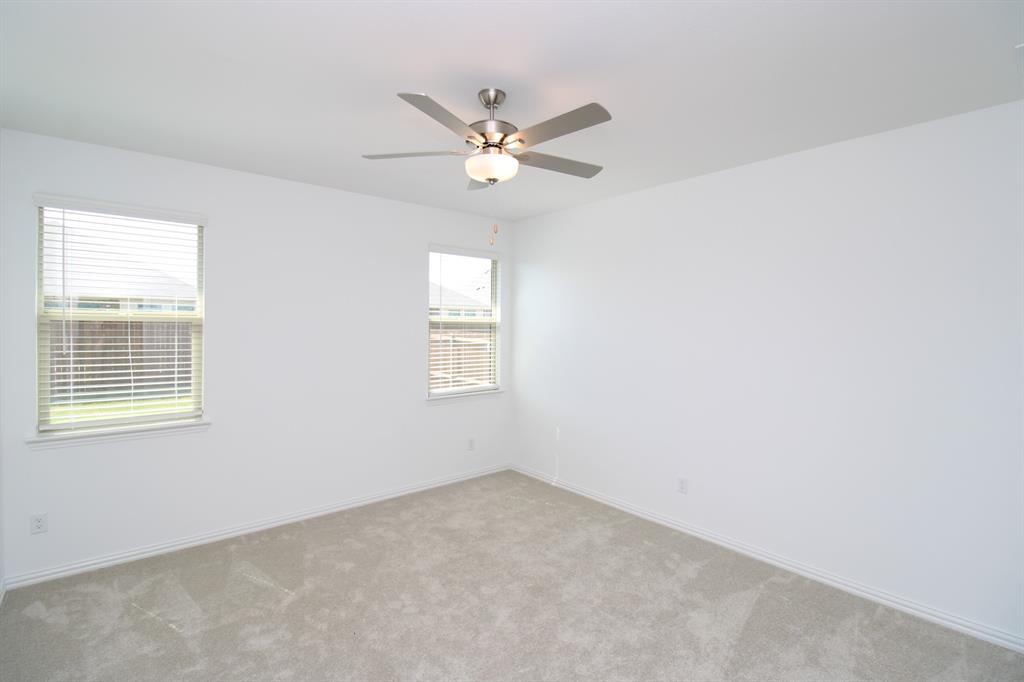 Neutral interior space featuring carpeted flooring, two windows with horizontal blinds, and a brushed-nickel ceiling fan with integrated lighting