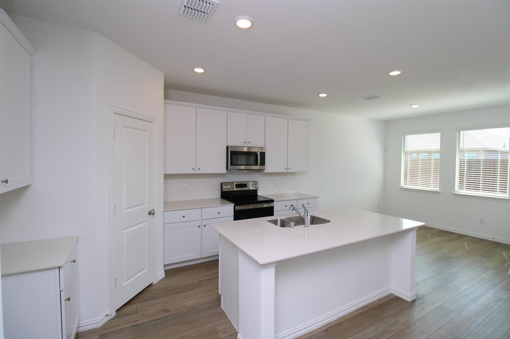 Kitchen featuring white cabinetry, quartz countertops, a central island with a double-basin sink, stainless steel appliances, and wood-finish flooring