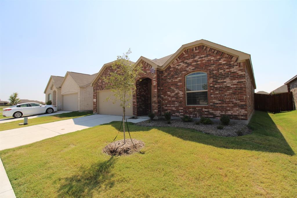 Brick exterior featuring a gabled roofline, arched window detail, concrete driveway, and front landscaping