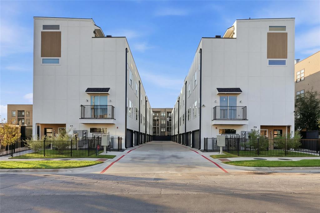 Contemporary multi-level residential structures featuring smooth white stucco facades, metal railing balconies, integrated garage entries, and wood-finish panel accents