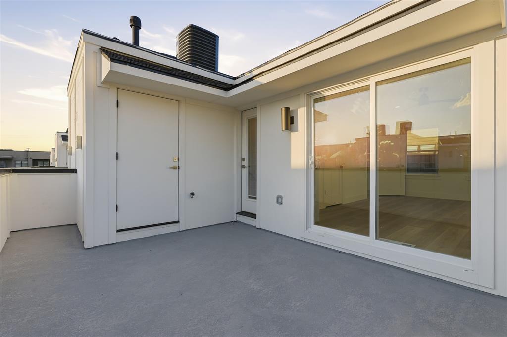 Rooftop terrace featuring concrete flooring, sliding glass door, exterior wall-mounted lighting, and neutral-toned siding