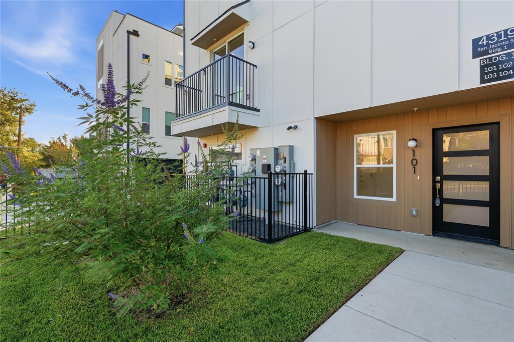 Modern exterior featuring white paneled siding, horizontal wood-toned accents, a second-story balcony with metal railings, and a contemporary glass-paneled front door
