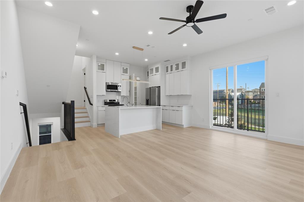 Open-concept interior featuring light wood-finish flooring, white shaker-style cabinetry, a central kitchen island, recessed lighting, and a sliding glass door