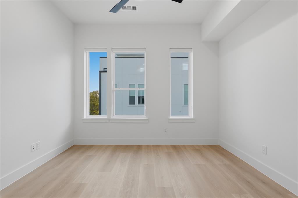 Neutral-toned space featuring wood-finish flooring, three oversized windows, and a ceiling-mounted fan