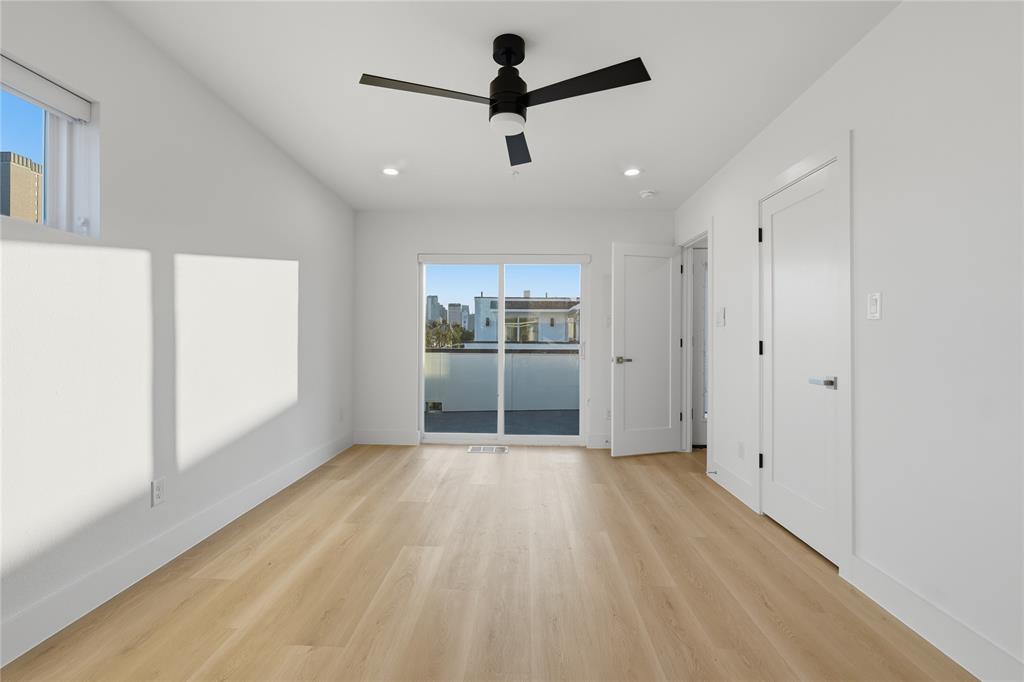 Wood-finish flooring, sliding glass door with access to a balcony, matte black ceiling fan, and recessed lighting