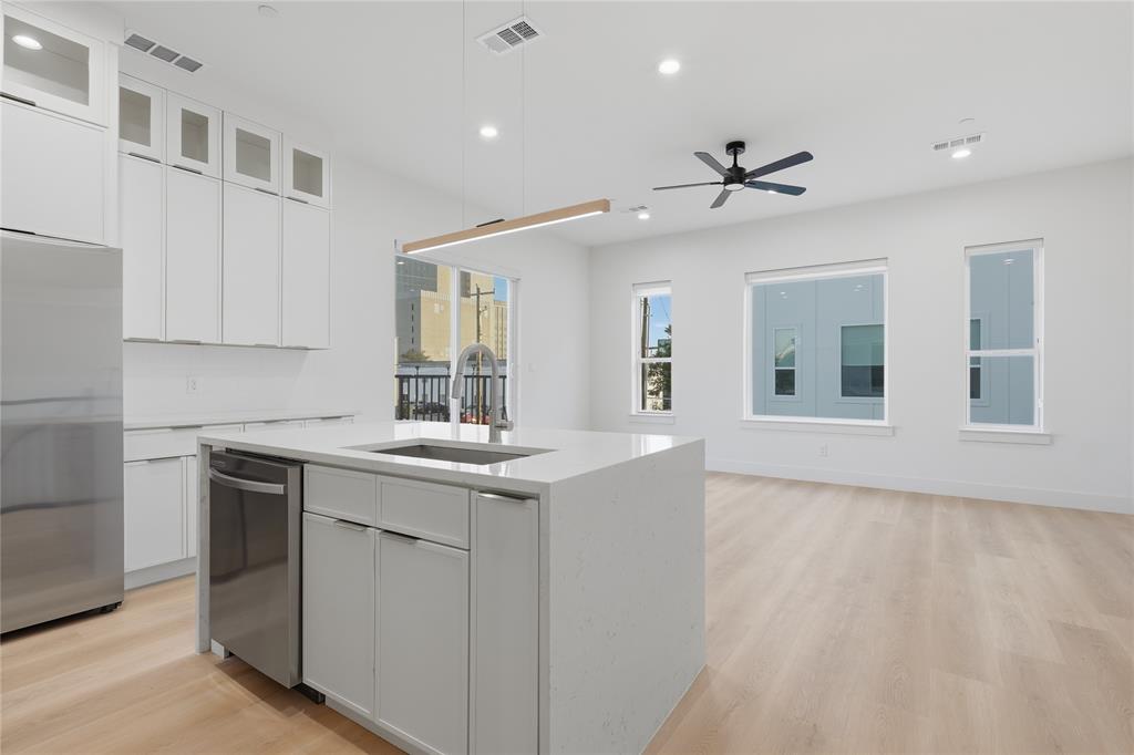 Kitchen featuring floor-to-ceiling white cabinetry, central island with stone-finish countertop, stainless steel appliance, wood-finish flooring, and recessed ceiling lighting