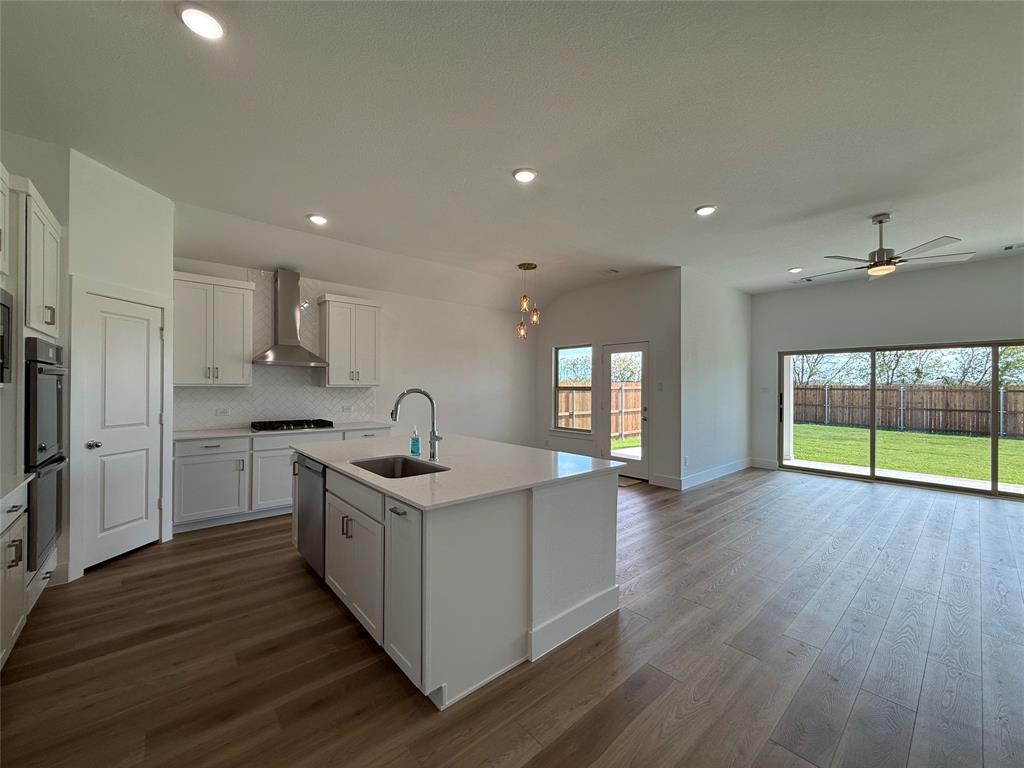 Kitchen featuring white shaker-style cabinetry, a central island with a quartz countertop, stainless steel appliances, wood-finish flooring, and large glass sliding doors