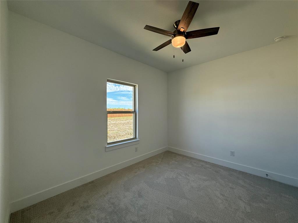 Neutral interior space featuring neutral wall-to-wall carpeting, a multi-blade dark wood-finish ceiling fan with integrated lighting, and a single window
