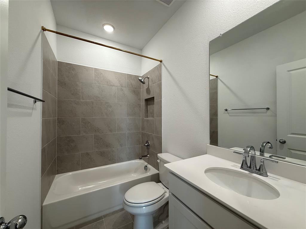 Bathroom featuring a vanity with a white countertop and oval under-mount sink, full-width mirror, and a tub-shower combination with grey tile surround and built-in recessed soap niche