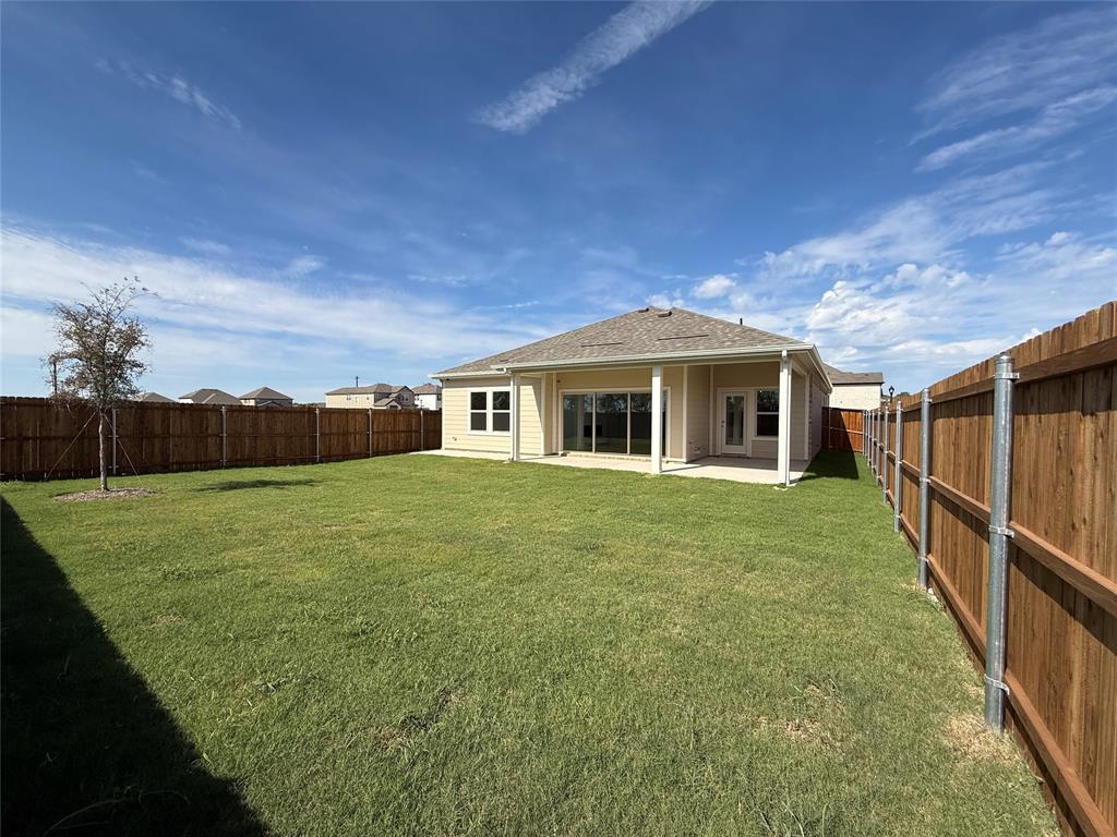 Rear exterior featuring a covered concrete patio, a full-height wood privacy fence, and a sodded lawn